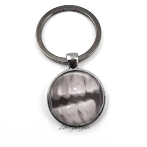 May include: A silver keychain with a round glass charm featuring a black and white x-ray image of teeth.