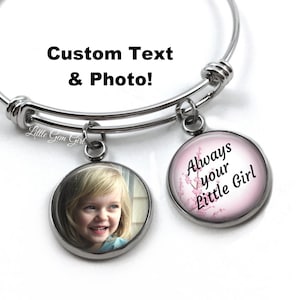 May include: A silver expandable bangle bracelet with two charms. One charm features a photo of a young girl, and the other charm has a pink background with white flowers and the text "Always your Little Girl".