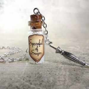 May include: A silver chain necklace with a small glass bottle charm. The bottle has a cork stopper and a label that reads "Spoonful of Sugar". The necklace also has a small silver charm shaped like an umbrella.