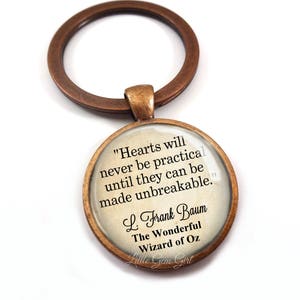 May include: A bronze-colored key chain with a round glass charm featuring a quote from L. Frank Baum's "The Wonderful Wizard of Oz": "Hearts will never be practical until they can be made unbreakable."