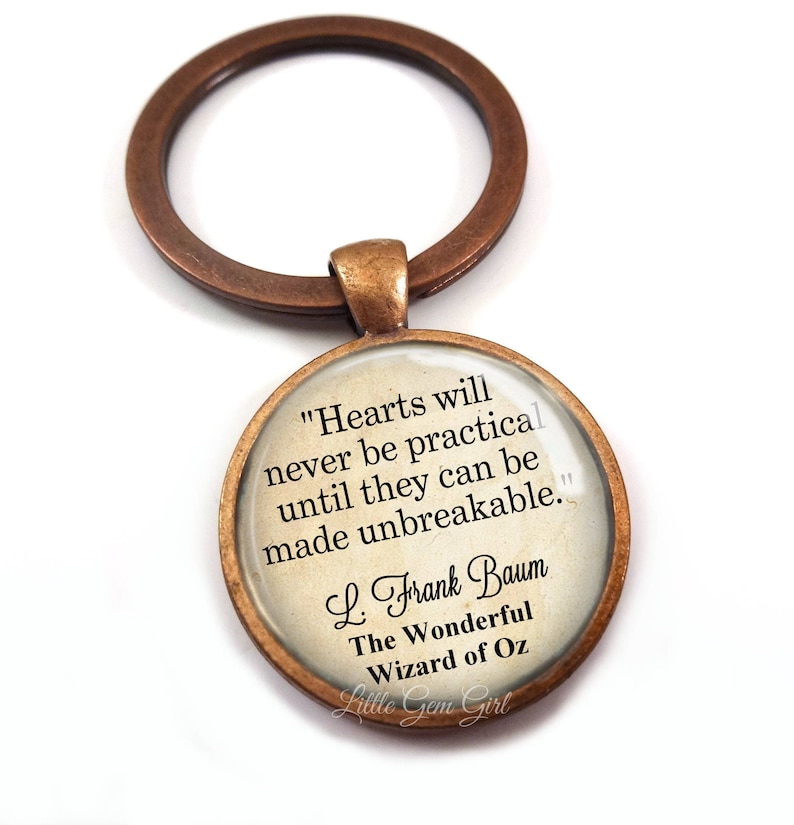 May include: A bronze-colored key chain with a round glass charm featuring a quote from L. Frank Baum's "The Wonderful Wizard of Oz": "Hearts will never be practical until they can be made unbreakable."