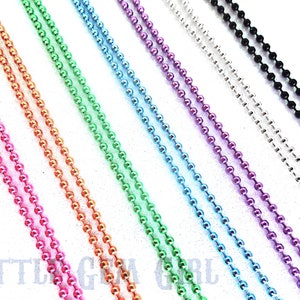 May include: Assortment of colorful metal chains, including pink, orange, green, blue, purple, silver, and black. The chains are made of small, round beads.