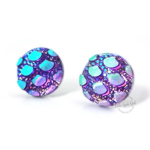 May include: A pair of iridescent purple and blue stud earrings with a textured, scaly design. The earrings are round and have a shiny finish.
