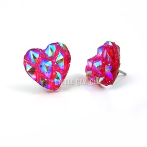 May include: A pair of heart-shaped earrings with a red base and iridescent glitter. The earrings are made of a clear material with a textured surface.