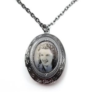 May include: A silver locket necklace featuring a black and white photograph of a woman. The locket is oval shaped and has an intricate design.