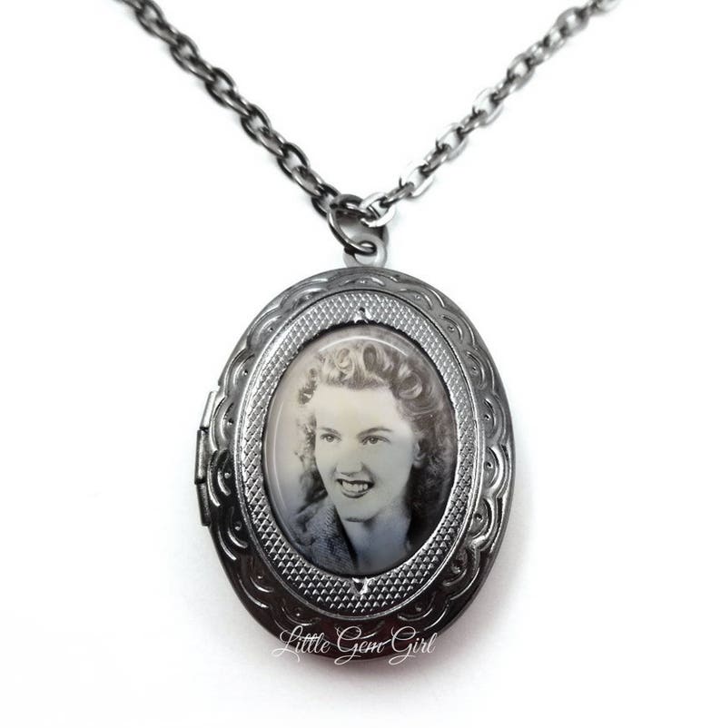 May include: A silver locket necklace featuring a black and white photograph of a woman. The locket is oval shaped and has an intricate design.
