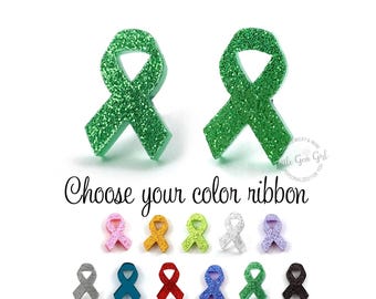 Op de afbeelding: Twee grote groene glitter awareness-lintspeldjes boven de tekst "Choose your color ribbon" en een collectie van twaalf kleinere lintspeldjes in diverse kleuren, waaronder roze, oranje, limoengroen, wit, paars, zilver, taling, rood, blauw, groen en zwart.