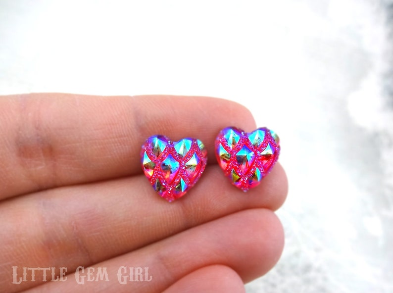 May include: A pair of pink heart-shaped earrings with a glittery, iridescent finish. The earrings have a geometric pattern and are a vibrant shade of pink.