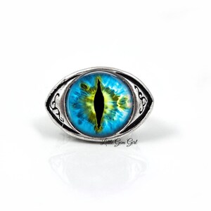 May include: A silver ring with a blue and yellow eye design. The eye has a black pupil and a yellow iris.