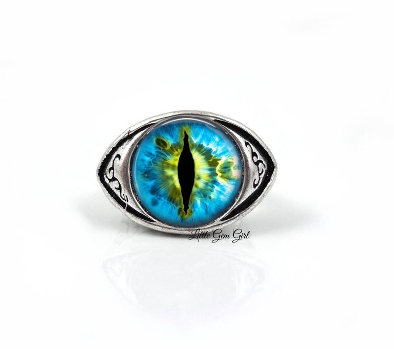 May include: A silver ring with a blue and yellow eye design. The eye has a black pupil and a yellow iris.