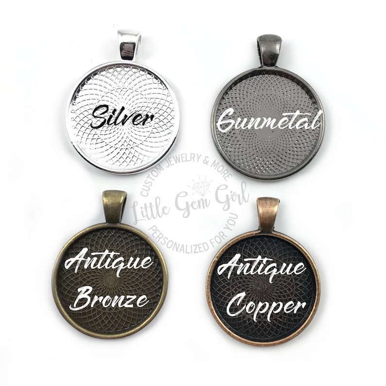 May include: Four round metal pendant blanks with different finishes: silver, gunmetal, antique bronze, and antique copper. Each blank has a raised rim and a textured surface. The text "Silver", "Gunmetal", "Antique Bronze", and "Antique Copper" is printed on each blank.