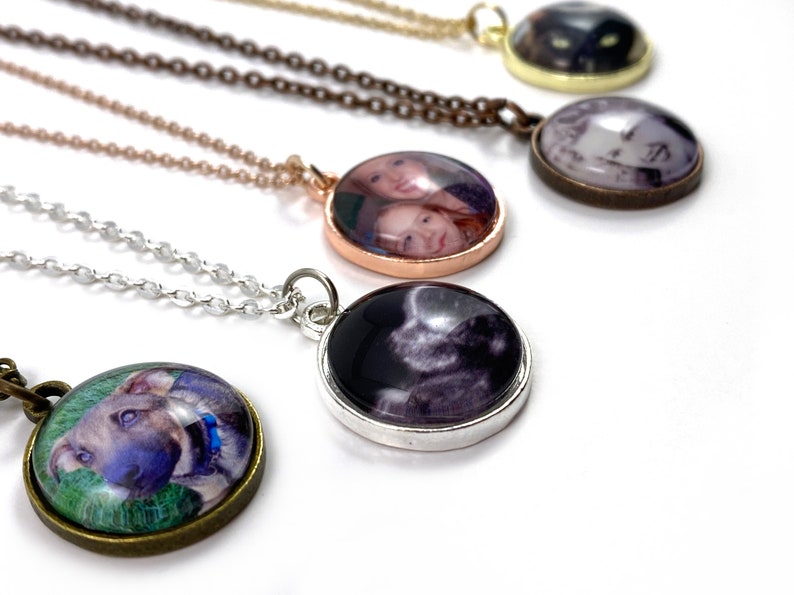 Puede incluir: Cinco collares con colgantes redondos de vidrio que muestran diferentes fotos. Los colgantes est&aacute;n unidos a cadenas plateadas, doradas y de bronce.