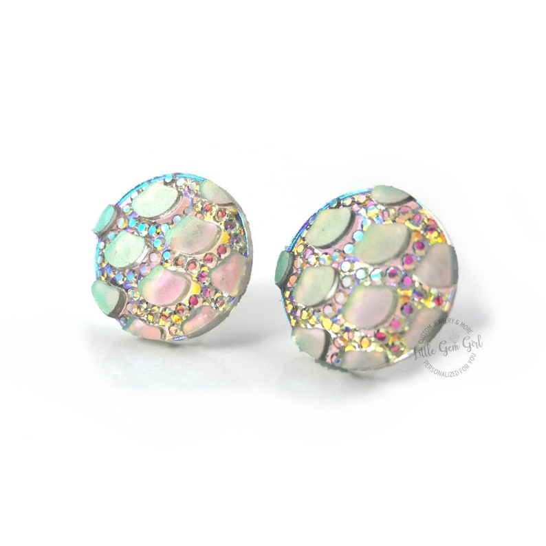 May include: A pair of iridescent round stud earrings with a mosaic design. The earrings are made of silver and have a light blue, pink, and green color scheme.