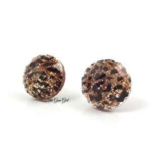 May include: A pair of gold and black glitter stud earrings with a leopard print design.