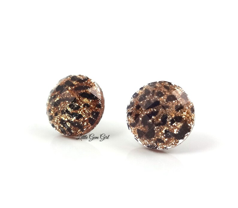 May include: A pair of gold and black glitter stud earrings with a leopard print design.