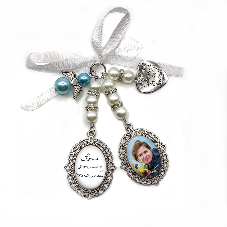 May include: A silver charm featuring a photo of a woman with the inscription "Love forever, Mama" on one side and a silver heart charm with the inscription "You are always in my heart" on the other. The charm is attached to a white ribbon and a string of white and blue beads.