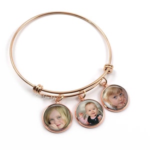 May include: Rose gold bangle bracelet with three round photo charms. Each charm features a different photo of a child.