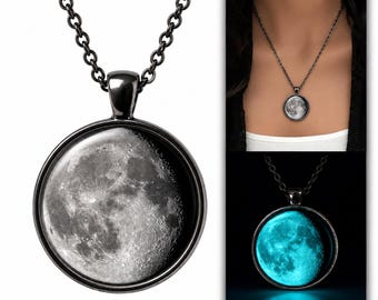 May include: A round pendant necklace featuring a detailed lunar surface image set in a black metal frame on a matching chain. The pendant displays a realistic moon crater design that glows with a bright cyan light in dark conditions.