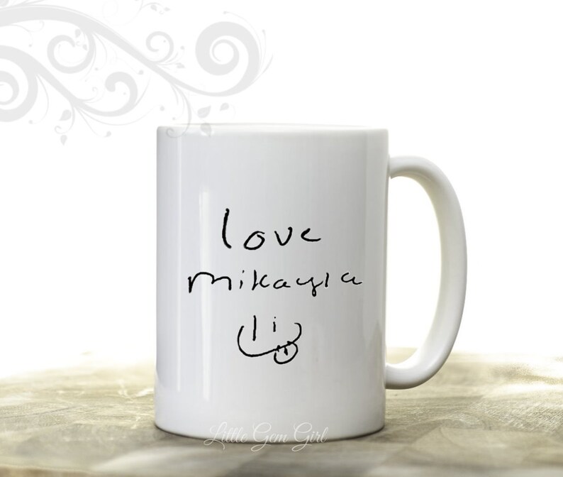 Może przedstawiać: Biały ceramiczny kubek z zakrzywionym uchwytem. Kubek ma odręczny tekst z napisem "love mikayla li" czarnym tuszem. Kubek ma błyszczące wykończenie i jest umieszczony na białym tle.