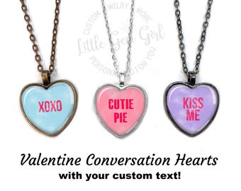 Op de afbeelding: Drie zilveren hartvormige kettingen met verschillende gekleurde glazen harten. De harten hebben de woorden "XOXO", "Cutie Pie" en "Kiss Me" in roze erop gedrukt.