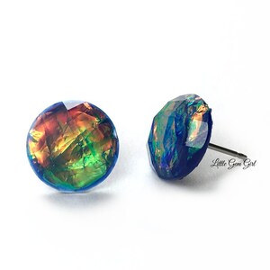 May include: A pair of iridescent blue stud earrings with a multi-coloured, iridescent, geometric design. The earrings are made of resin and have a silver post.