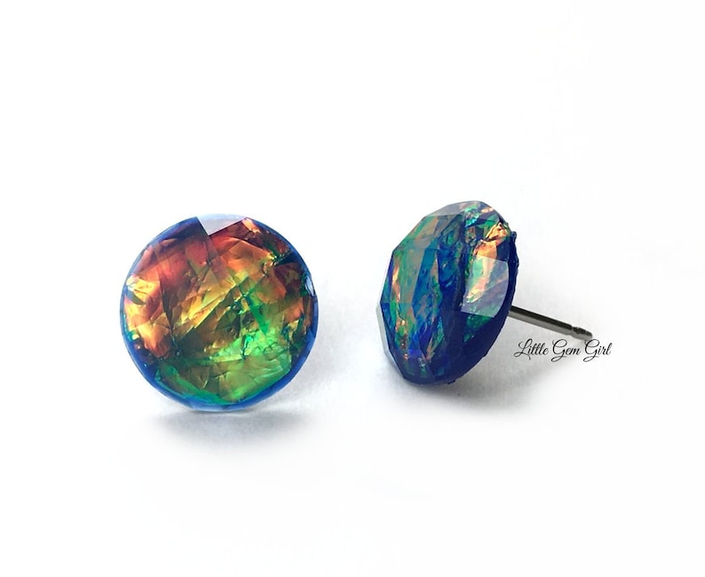 May include: A pair of iridescent blue stud earrings with a multi-coloured, iridescent, geometric design. The earrings are made of resin and have a silver post.