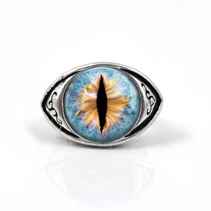 May include: A silver ring with a blue and yellow eye design. The eye has a black pupil and a white iris.