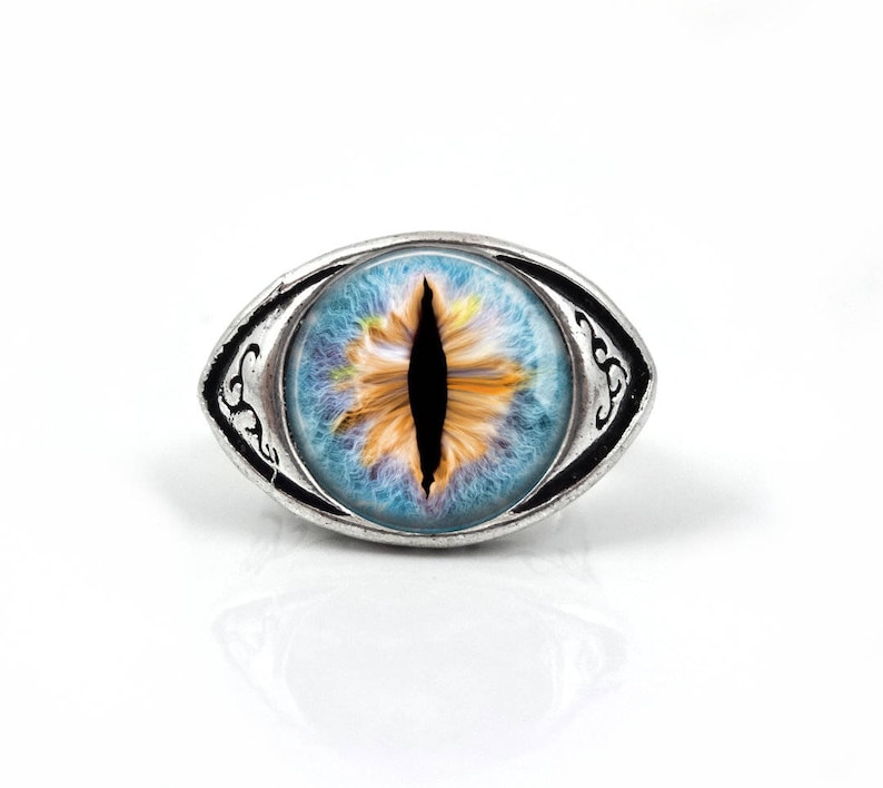 May include: A silver ring with a blue and yellow eye design. The eye has a black pupil and a white iris.