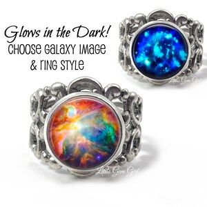 May include: Two silver rings with a galaxy image inside the ring. The ring on the left has a colorful galaxy image and the ring on the right has a blue galaxy image. Both rings glow in the dark.