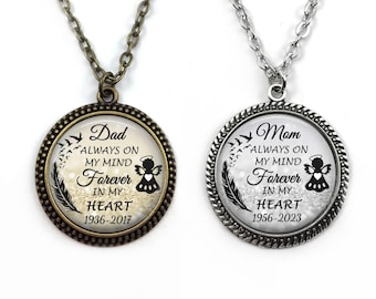 Könnte beinhalten: Zwei silberfarbene Halsketten mit Glasanhängern. Die Anhänger zeigen ein Schwarzweißbild eines Engels mit einer Feder und dem Text "Dad Always on My Mind Forever in My Heart 1936-2017" und "Mom Always on My Mind Forever in My Heart 1956-2023".