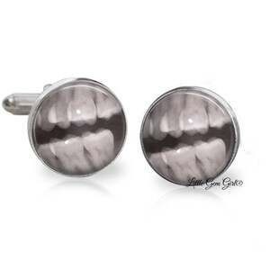May include: A pair of silver cufflinks with a black and white x-ray image of teeth on each cufflink. The cufflinks are round and have a silver metal frame.
