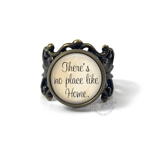May include: A bronze ring with a round, white cameo featuring the text "There's no place like Home."