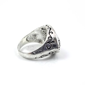 May include: A silver ring with an ornate design. The ring is engraved with a swirling pattern.