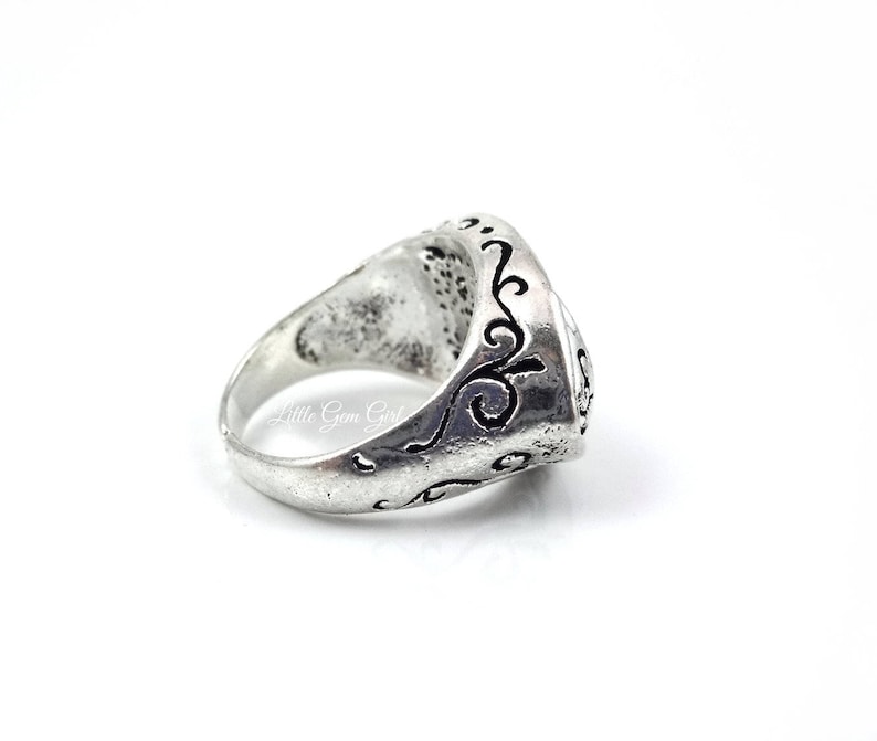 May include: A silver ring with an ornate design. The ring is engraved with a swirling pattern.