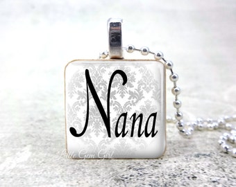 May include: A silver chain necklace with a square pendant featuring a white damask pattern and the word "Nana" in black script.