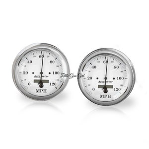 May include: Two white car gauges with chrome bezels. The gauges are labeled "Auto Meter" and "MPH". The needles are pointing to 60.