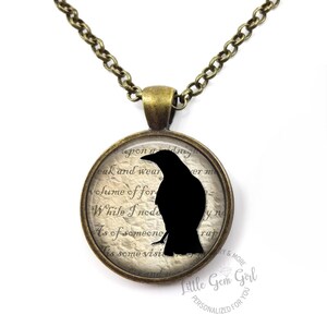May include: A bronze chain necklace with a round pendant featuring a black silhouette of a raven on a vintage-style background with text that reads "eak and wear volume of for While I'noda As of someone Es some visit ver m yng rap".