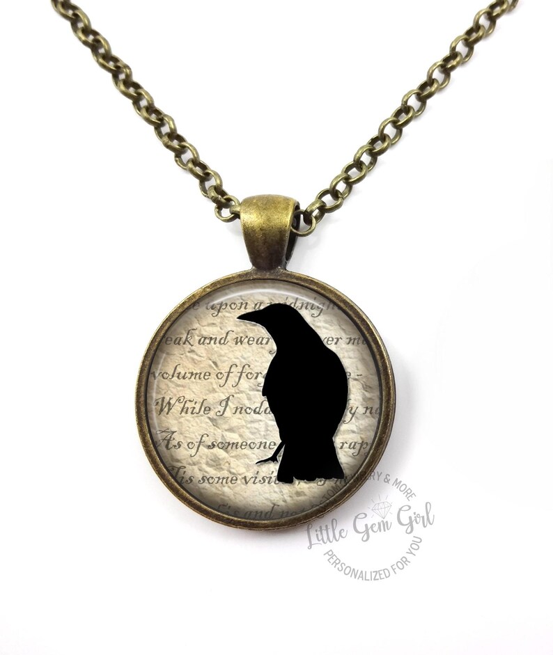 May include: A bronze chain necklace with a round pendant featuring a black silhouette of a raven on a vintage-style background with text that reads "eak and wear volume of for While I'noda As of someone Es some visit ver m yng rap".