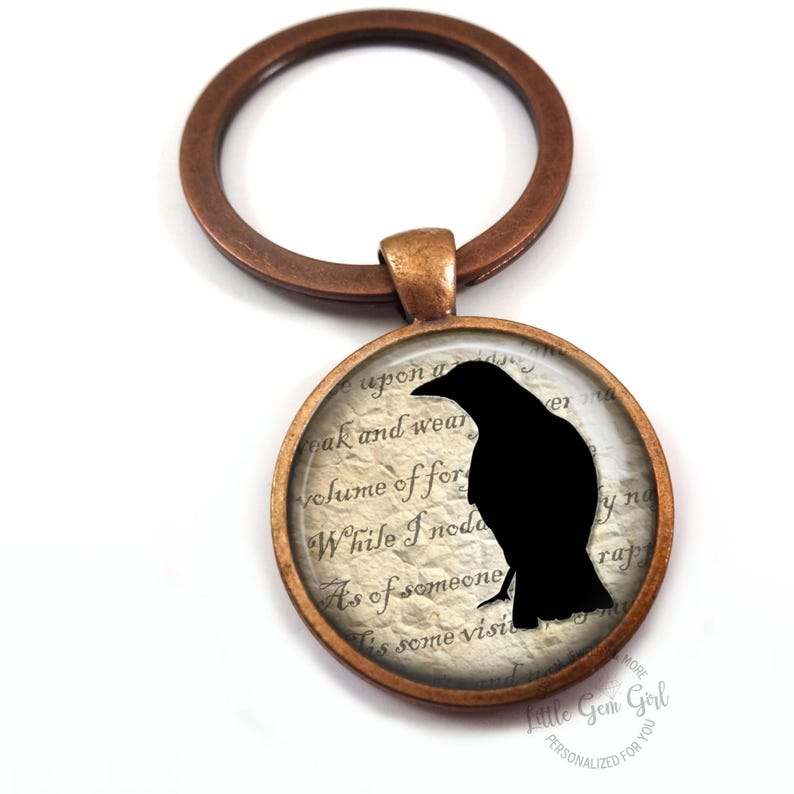 May include: A bronze key chain with a round glass charm featuring a black silhouette of a raven on a vintage paper background. The text on the paper reads "While I nod as of someone's visit".