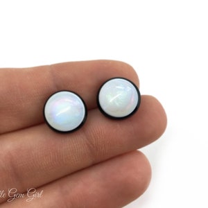 Pu&ograve; includere: Un paio di orecchini a perno rotondi bianchi iridescenti con montature in metallo nero.