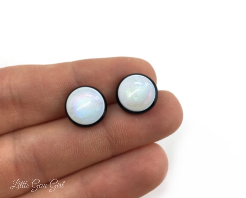Pu&ograve; includere: Un paio di orecchini a perno rotondi bianchi iridescenti con montature in metallo nero.