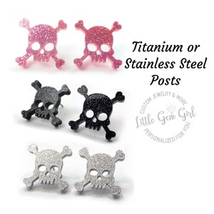 May include: Three pairs of skull and crossbones earrings with glitter. The earrings are pink, black, and silver. The text on the image reads "Titanium or Stainless Steel Posts Custom Jewelry & More Little Gem Girl Personalized for You".