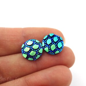 May include: A pair of blue and green iridescent stud earrings with a patterned design. The earrings are round and have a textured surface.