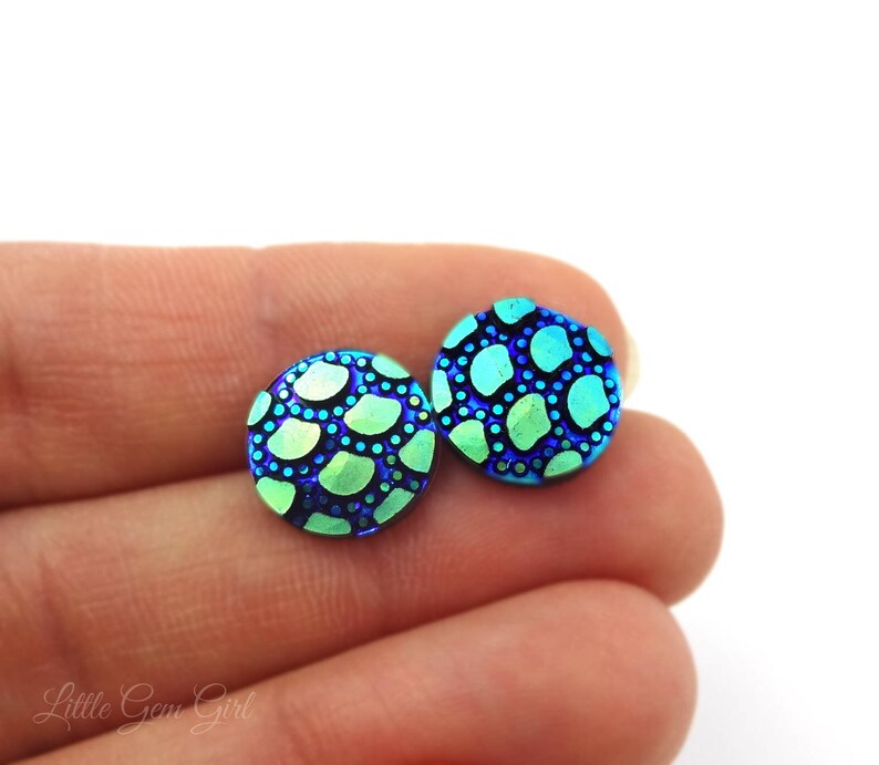 May include: A pair of blue and green iridescent stud earrings with a patterned design. The earrings are round and have a textured surface.