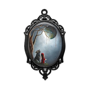 Könnte beinhalten: Ein ovaler Rahmen aus schwarzem Metall mit einem Glas-Cameo, das einen Wolf und ein Mädchen in einem roten Kapuzenmantel zeigt, die zu einem Halbmond in einem verschneiten Wald aufblicken.