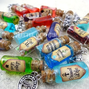 May include: A collection of small glass bottles with cork stoppers and labels. The bottles contain various colorful liquids and glitter. Some of the labels include text such as "Eat Me", "Mermaid Tears", "Bibbid Bobbid Boo", "Liquid Luck", and "Life Eternal".