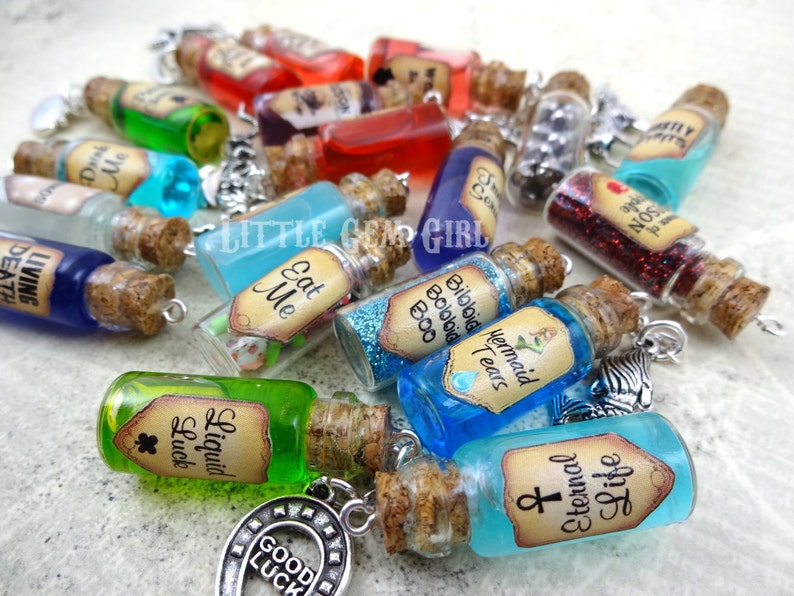 May include: A collection of small glass bottles with cork stoppers and labels. The bottles contain various colorful liquids and glitter. Some of the labels include text such as "Eat Me", "Mermaid Tears", "Bibbid Bobbid Boo", "Liquid Luck", and "Life Eternal".