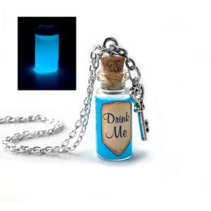 May include: A silver chain necklace with a blue glass bottle pendant that says "Drink Me" on a vintage label. The bottle has a cork stopper and a silver key charm. The bottle glows blue in the dark.