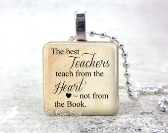 Op de afbeelding: Een vierkante hangerketting met een zilverkleurige beugel en kogelketting. De hanger toont de tekst "The best Teachers teach from the Heart ~ not from the Book." in zwarte letters op een beige achtergrond.