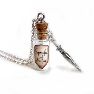 May include: A silver chain necklace with a small glass bottle charm. The bottle has a cork stopper and a label that reads "Spoonful of Sugar". A silver charm shaped like an umbrella hangs from the bottle.